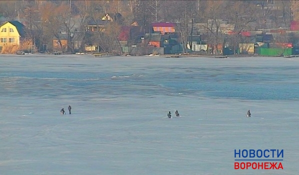 Рыбаки сидят на льду у открытой воды.